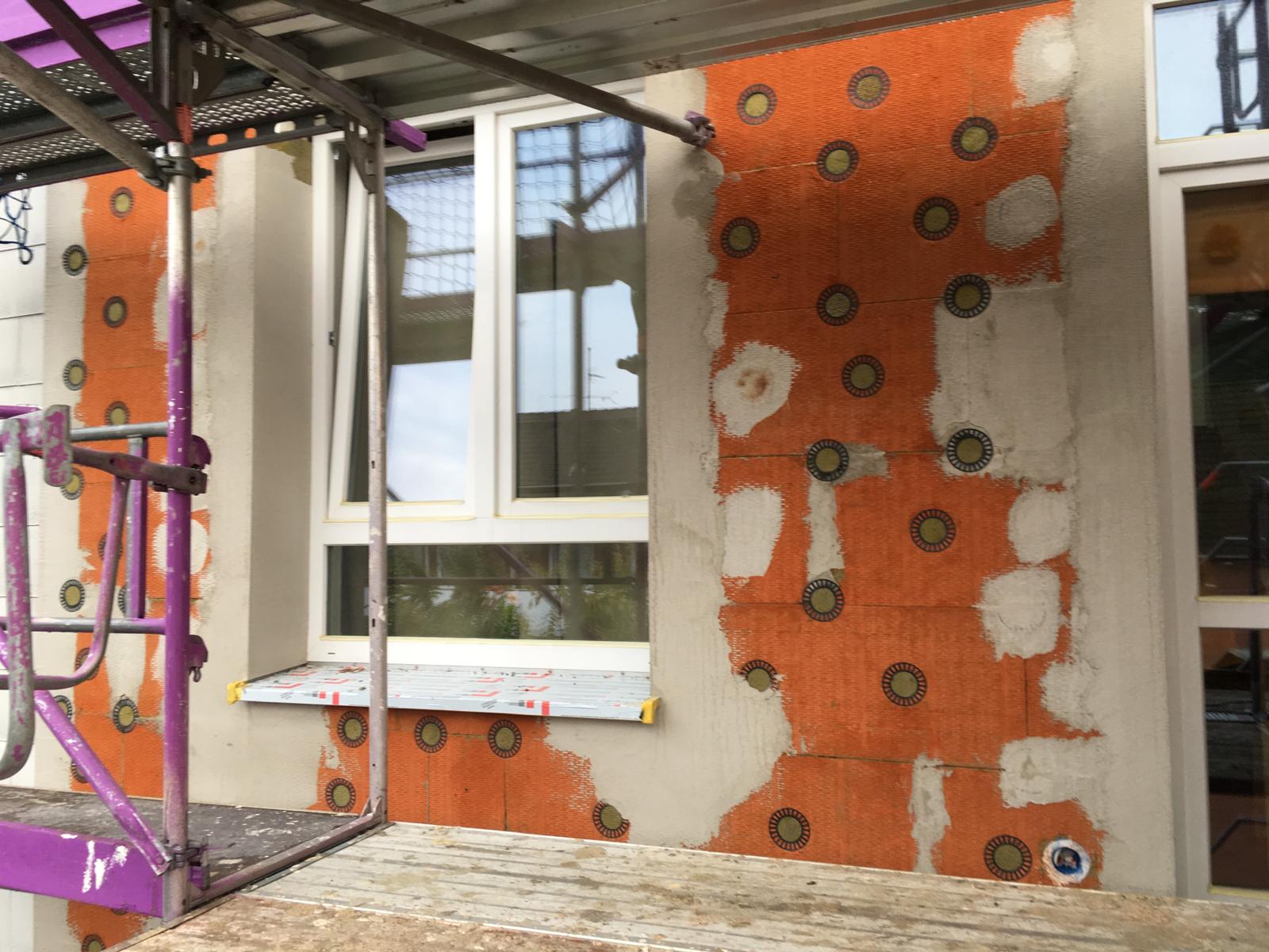 Fassadendämmung mit orangenen Dämmplatten, Dübeln und beginnendem Unterputz