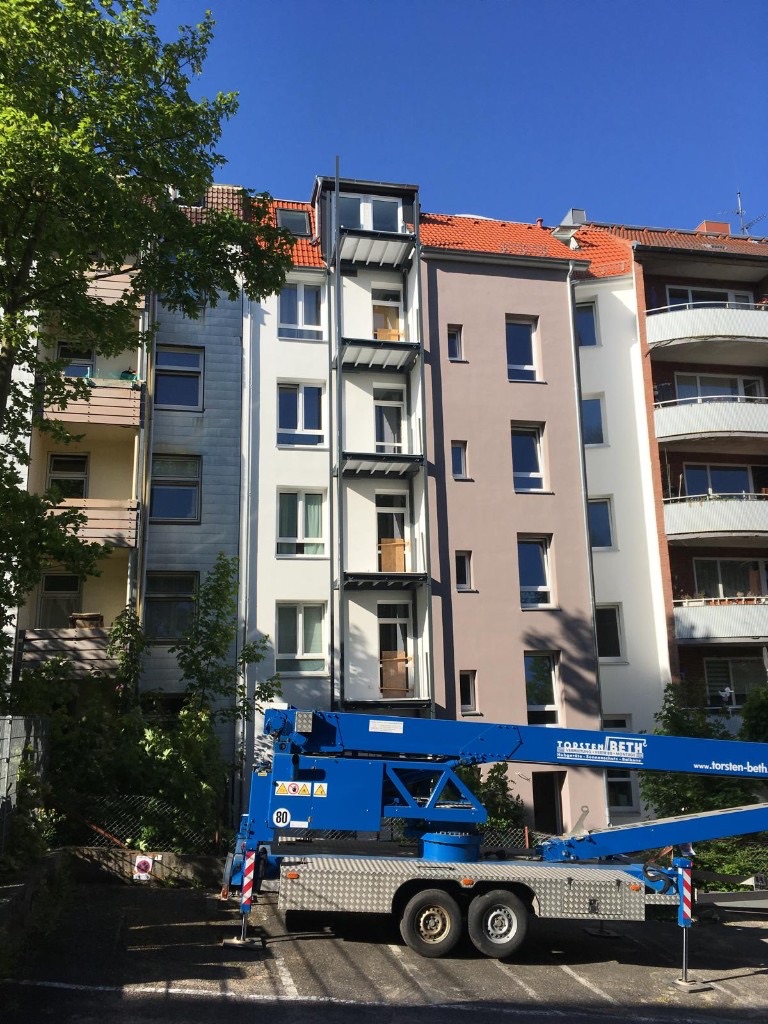 Frisch gestrichene Fassade eines Mehrfamilienhauses in Weiß und Taupe mit Arbeitslift